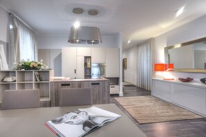 A modern kitchen with white cabinets, a built-in oven, and a dining area with a table and chairs. - Il Savoia (Cagliari)