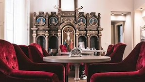 Un comedor con una mesa redonda, sillas tapizadas en terciopelo rojo y un fondo decorativo con pinturas religiosas.