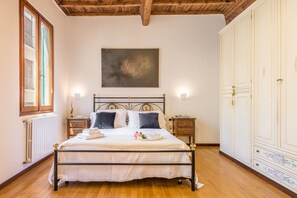 Un dormitorio con cama, piso de madera, paredes blancas, un cuadro y un armario.