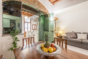 Comedor con una mesa de madera, un cuenco de fruta y un arco verde que da a una cocina.