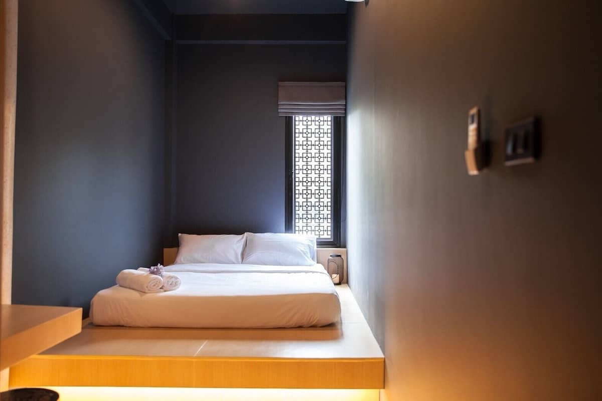 Quarto com cama, janela com persiana estampada e mesa de cabeceira.