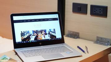 A laptop on a wooden desk with a book and a pen beside it.