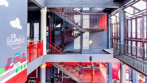 A multi-level interior with red railings, staircases, and a large window on the right. - Cloud on Saladaeng Silom Hostel Bangkok (Bangkok)