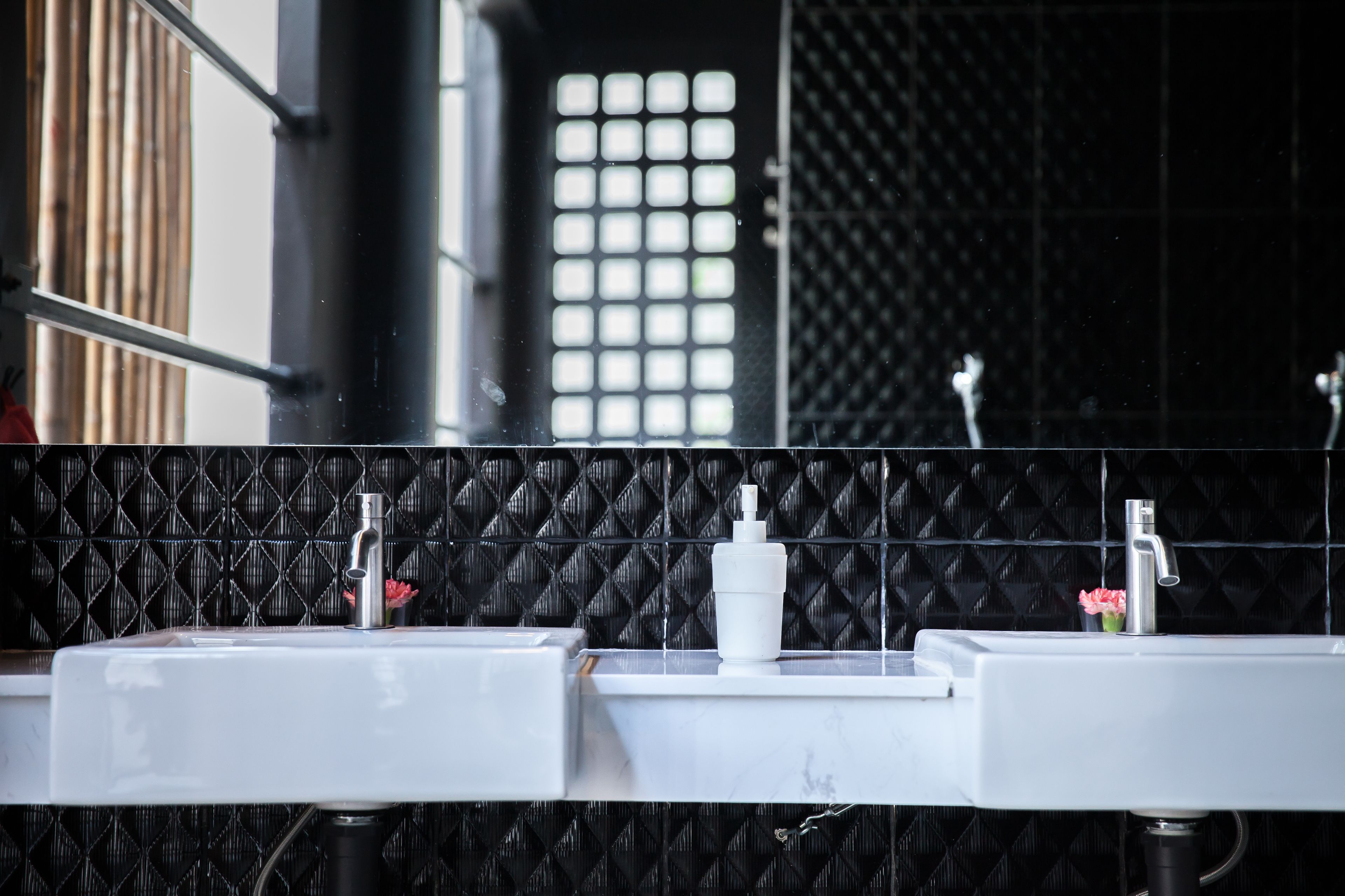 Une salle de bain avec deux lavabos, un miroir et un mur noir à texture.