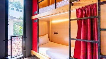 A bunk bed room with a window, a red curtain, and a view of a building outside.