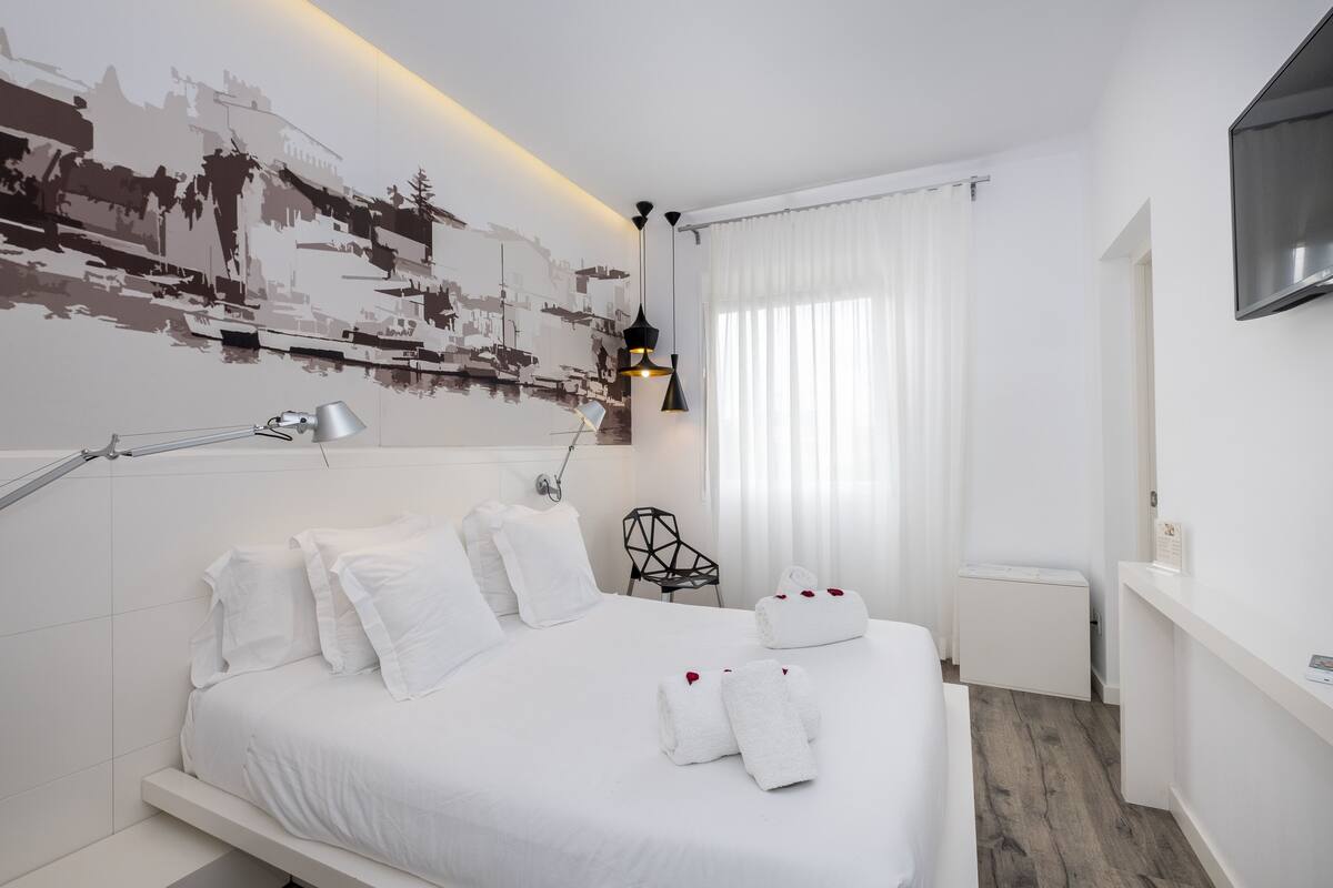 Una habitación de hotel moderna con una cama grande, un escritorio, una silla, un televisor de pantalla plana y una lámpara de pared.