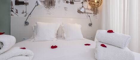 A neatly made bed with white linens, a wall mural of a coastal scene, and a decorative light fixture.