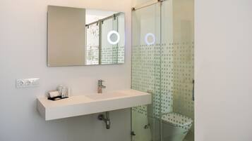 Un baño moderno con lavamanos blanco, espejo y cabina de ducha de vidrio.