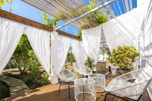 Une terrasse extérieure dotée de parasols blancs, de chaises en osier et de plantes en pot.