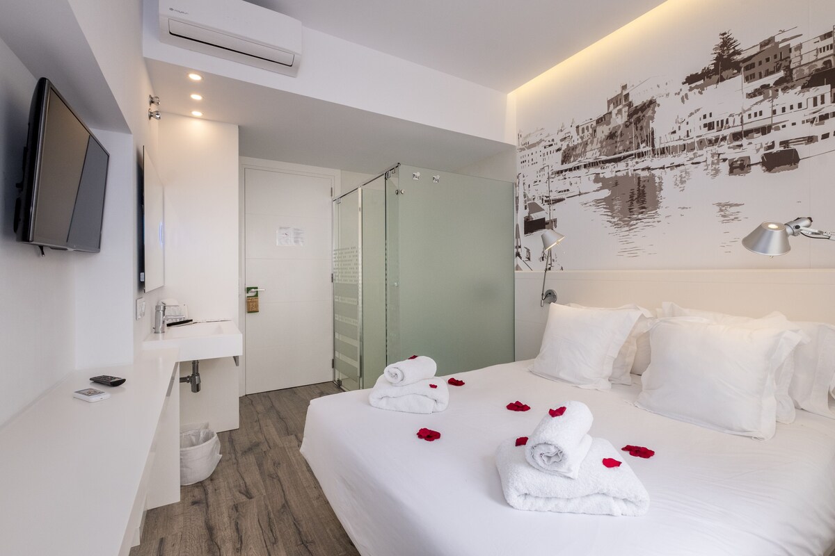 Hotelkamer met een bed, witte handdoeken, een douche, een wandtv en een muurschildering van een stadsgezicht.
