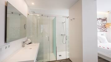 Een moderne badkamer met een douchecabine van glas, een wit wastafelmeubel en een bed met een witte dekbedovertrek.