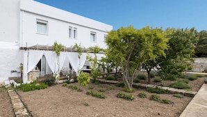 Een wit gebouw met een tuin ervoor, inclusief een boom en verschillende planten.