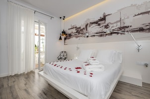 Un dormitorio moderno con una cama grande, ropa de cama blanca y pétalos de rosa sobre la cama.