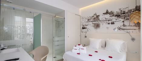 A hotel room with a bed, a desk, and a glass shower enclosure.