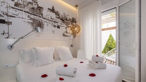A hotel room with a bed, white linens, a cityscape mural, a desk, and a view through a glass door. - Hotel Abril 37 (Ciutadella de Menorca)