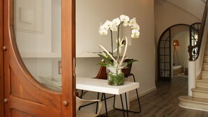 A modern interior with a wooden door, a white table with a vase of white orchids, and a staircase with a metal railing. - Hotel Abril 37 (Ciutadella de Menorca)