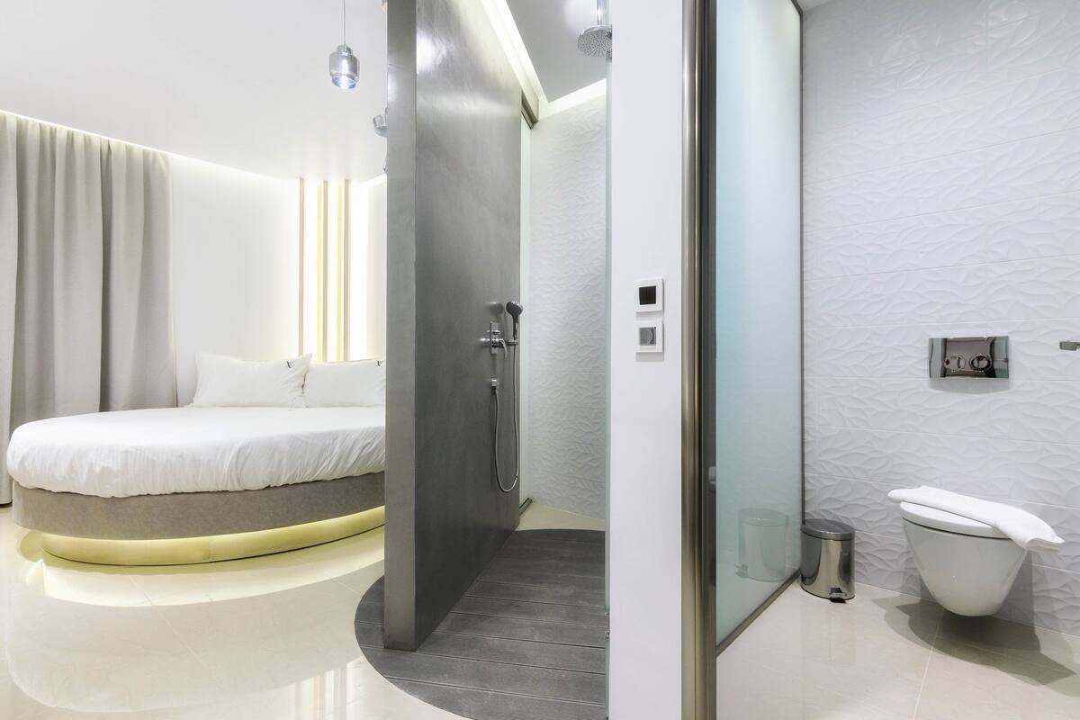 A modern bedroom with a curved bed, a shower, and a toilet in a compact bathroom.