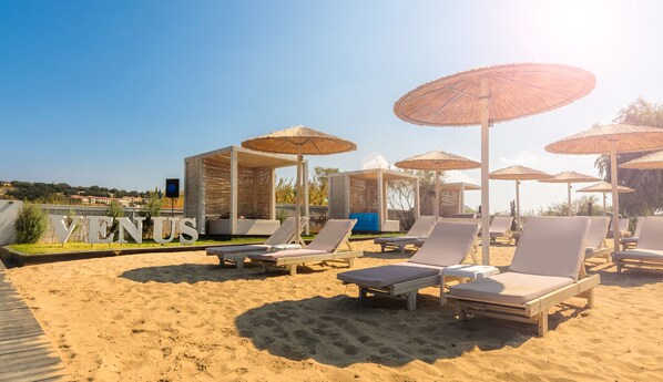 A beach with sun loungers and thatched umbrellas, a wooden deck, and a sign reading "VENUS". - Venus Resort (Zakynthos)
