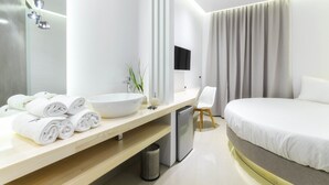 A modern hotel room with a large bed, a bedside table with a sink and towel rolls, a small fridge, and a TV mounted on the wall. - Venus Resort (Zakynthos)