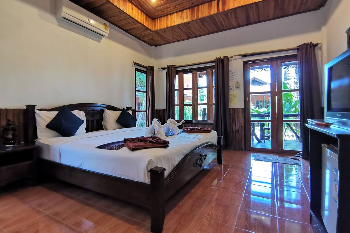 Quarto de hotel com uma cama grande, teto de madeira e uma televisão sobre um suporte.