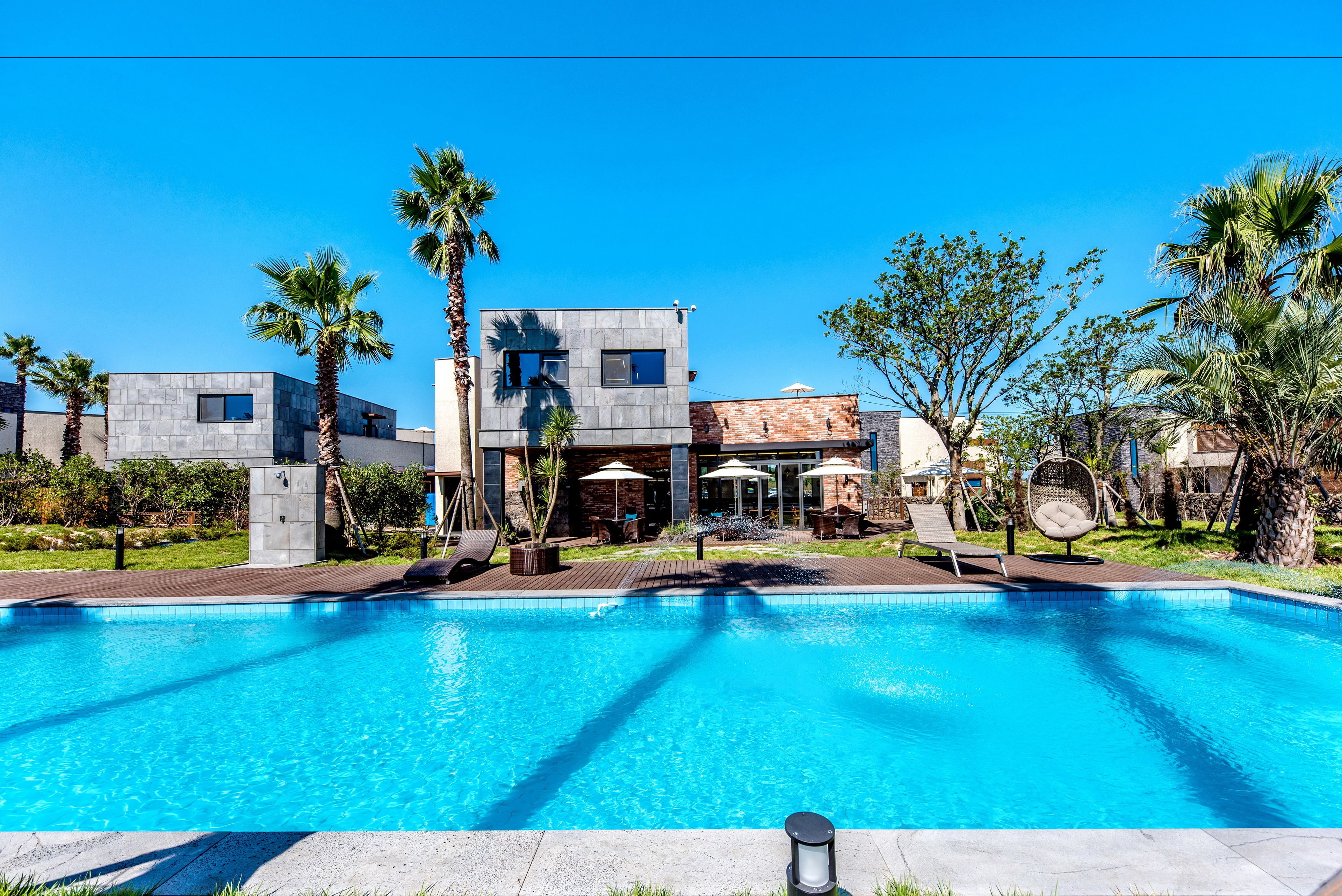 A modern hotel with a swimming pool, palm trees, and outdoor seating areas.