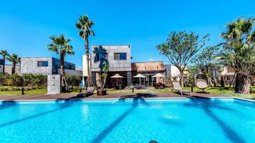 A modern hotel with a swimming pool, palm trees, and outdoor seating areas.