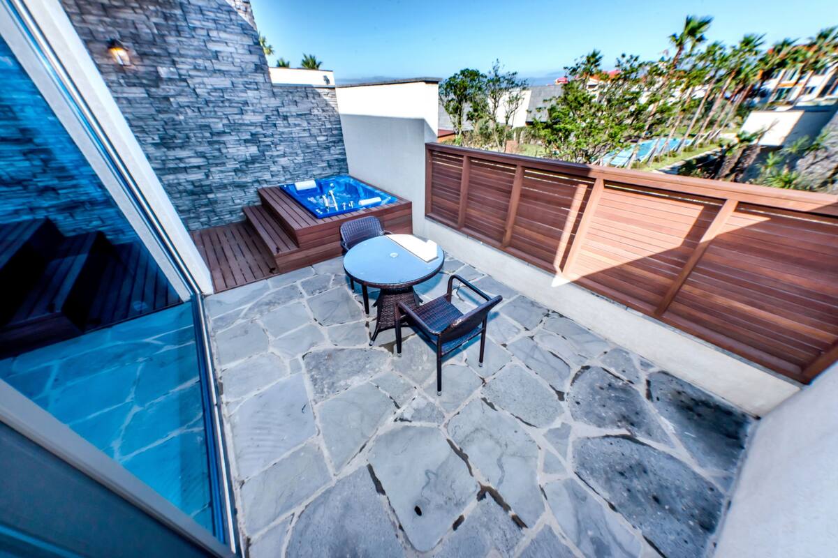 A stone patio with a hot tub, a round table, and chairs.