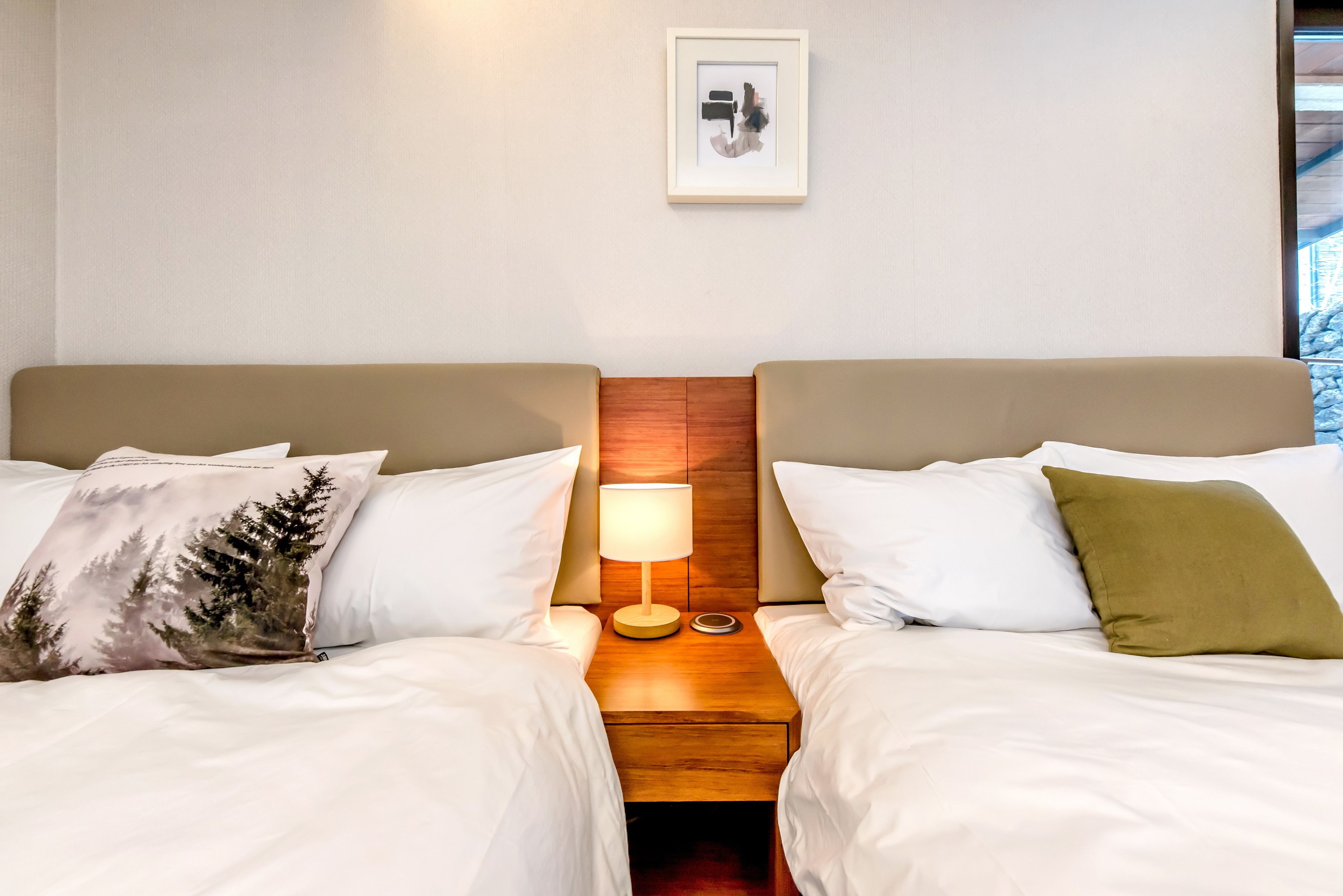 Ein Hotelzimmer mit zwei Betten, einem Nachttisch mit Lampe und einem gerahmten Bild an der Wand.