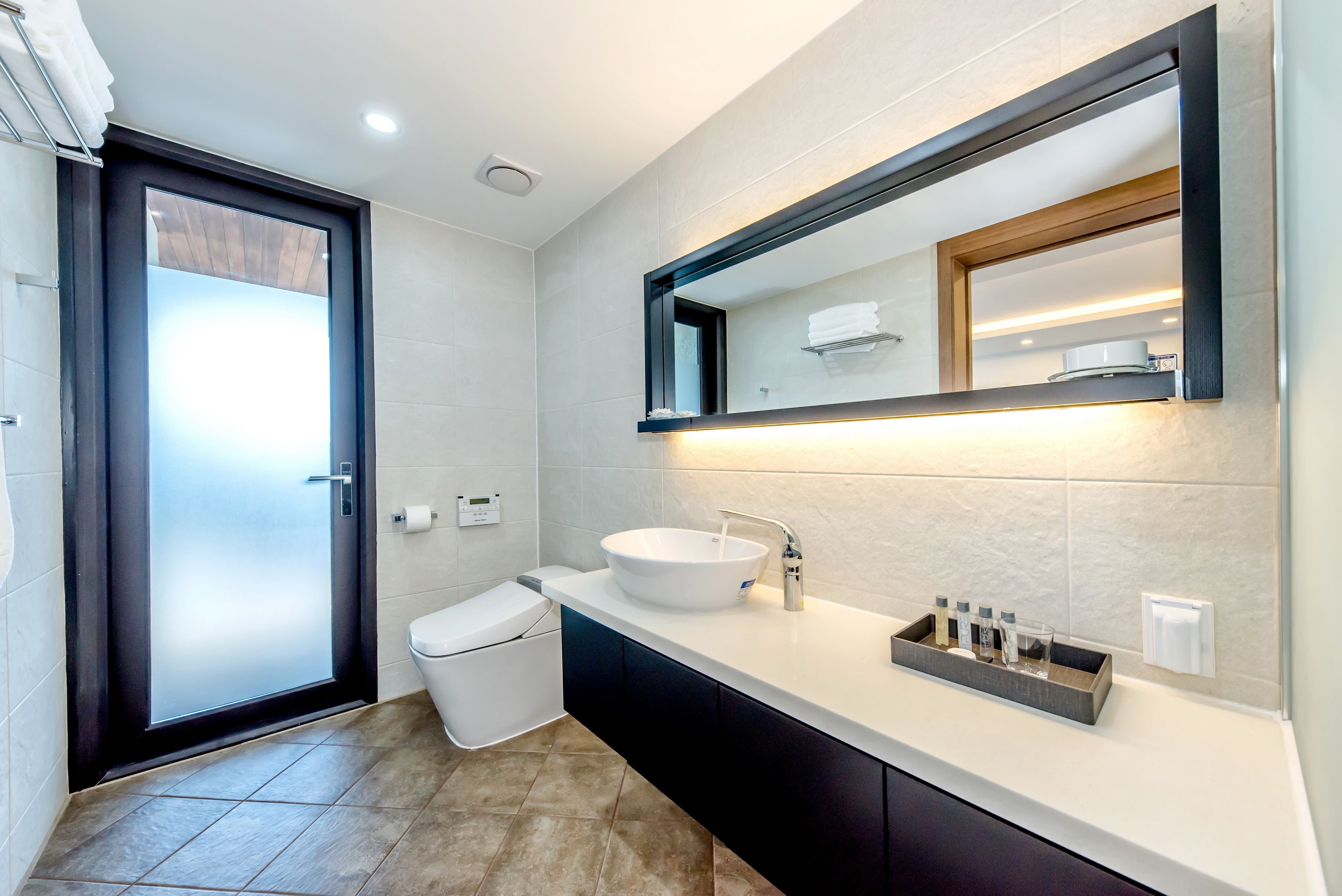 A modern bathroom with a large mirror, white sink, and dark cabinetry.
