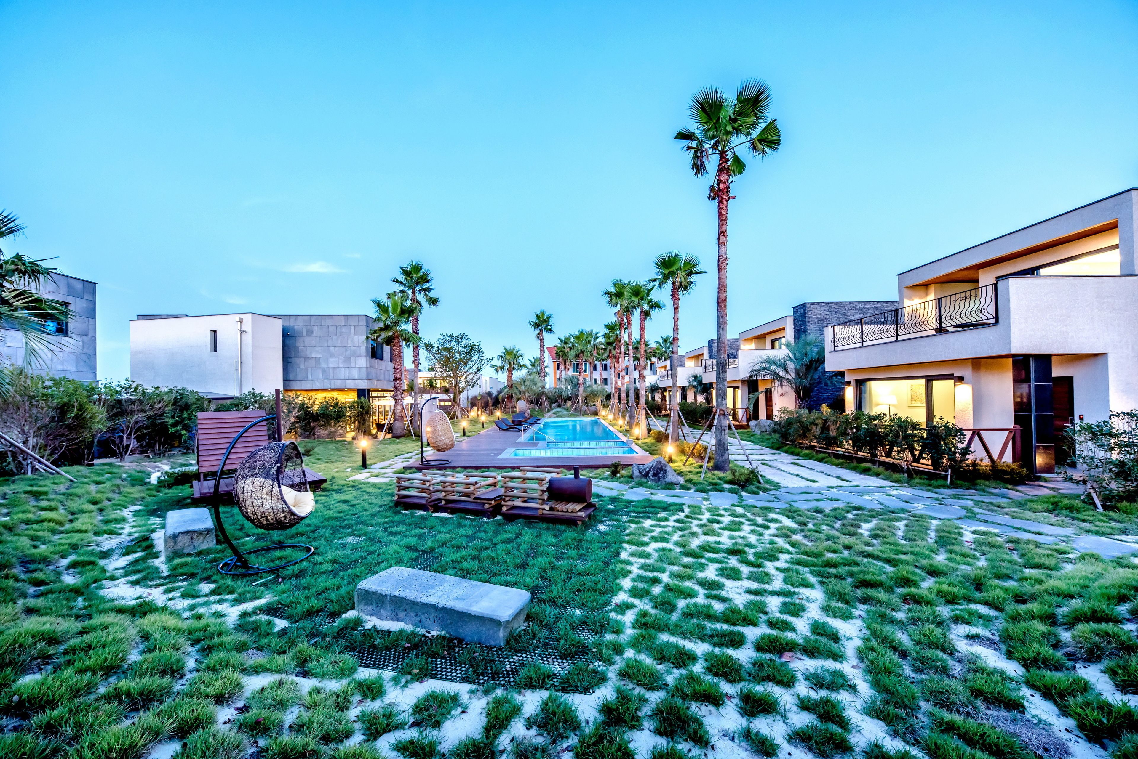 Ein modernes Resort mit Schwimmbad, Palmen und einem gepflegten Rasen.