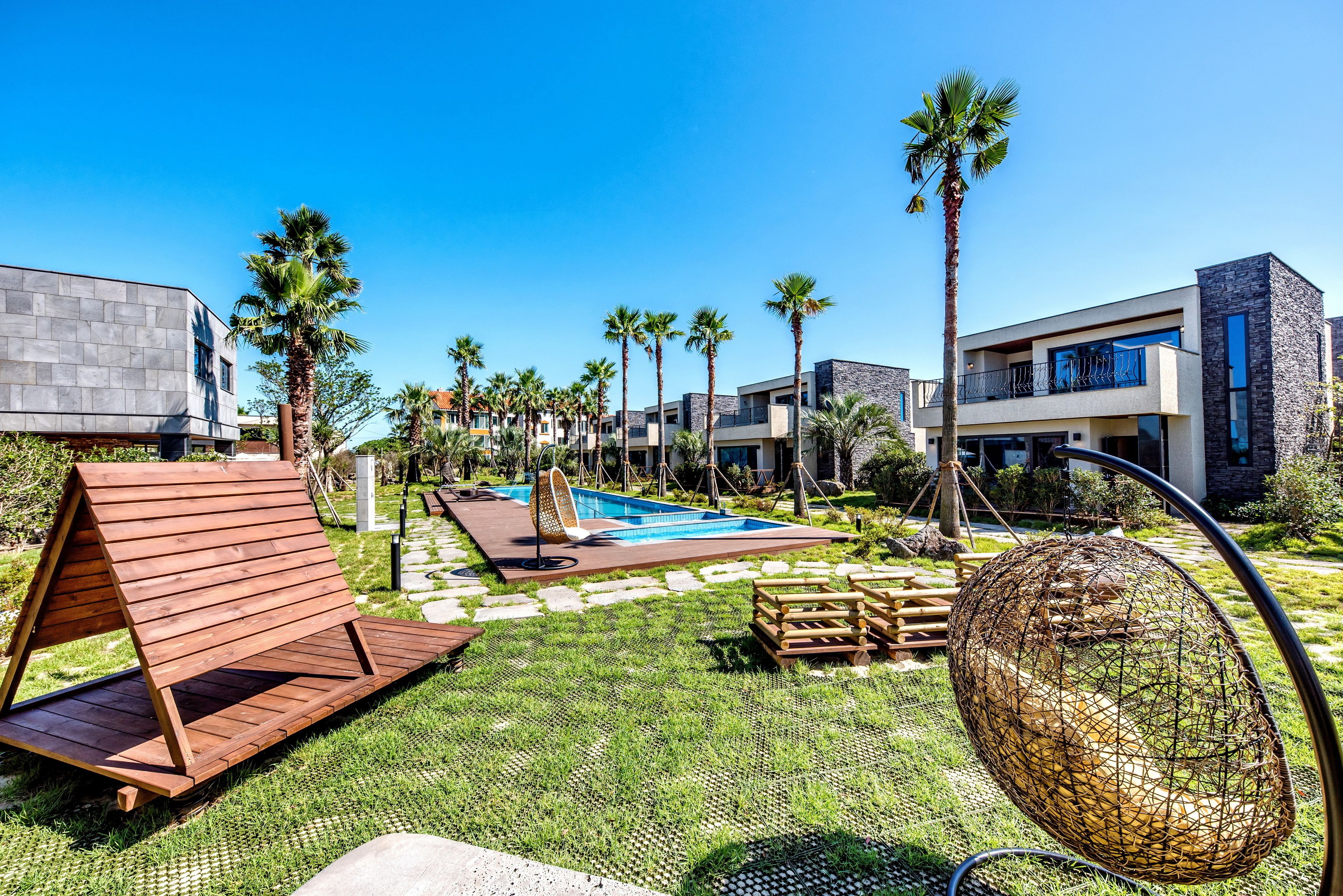 Een modern resort met een zwembad, palmbomen en een houten terras.