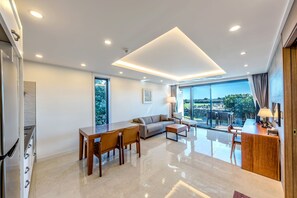 Una sala de estar moderna con sofá, mesa de comedor y sillas, un área de cocina y un amplio ventanal con vistas al exterior.