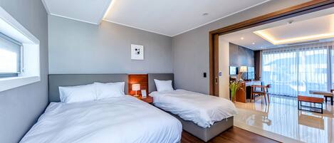 A modern hotel room with two beds, a desk, and a balcony with a view.