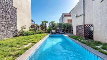 A swimming pool with a stone wall on one side and a modern building on the other.