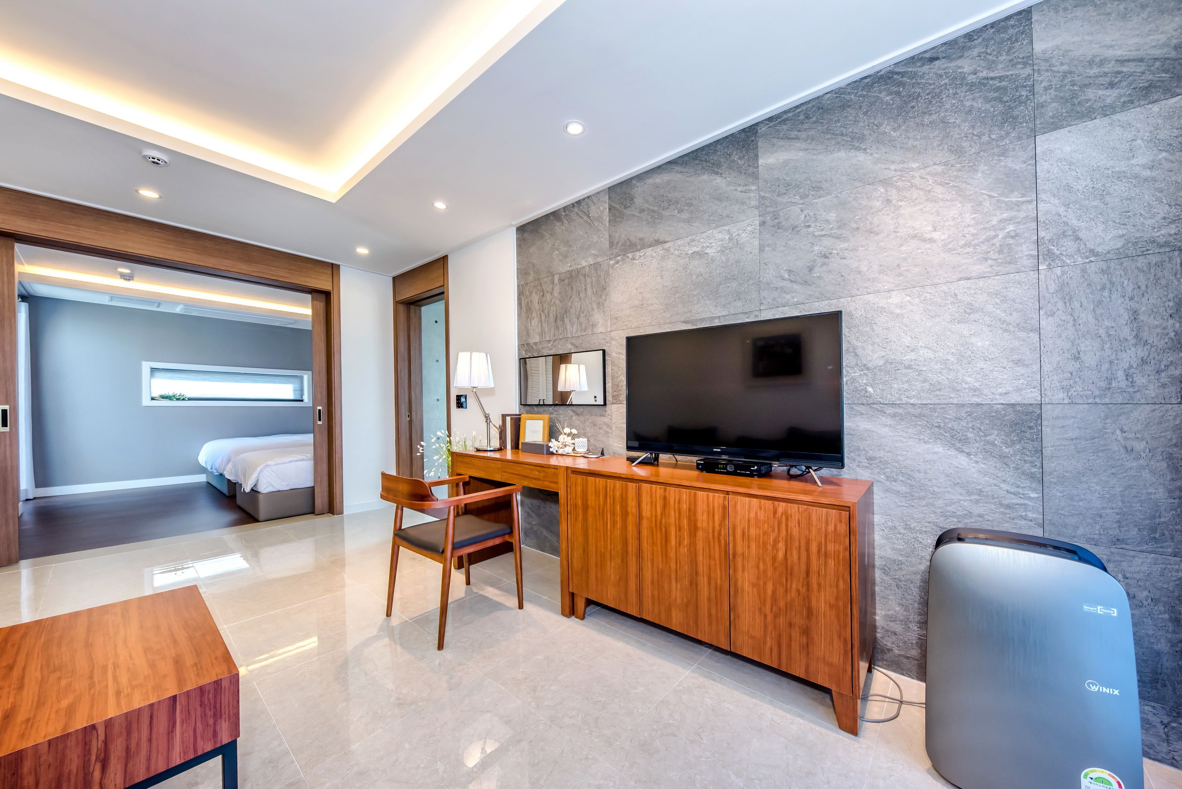 Une chambre d’hôtel moderne dotée d’un bureau en bois, d’un téléviseur à écran plat, d’un minibar et d’un grand miroir.