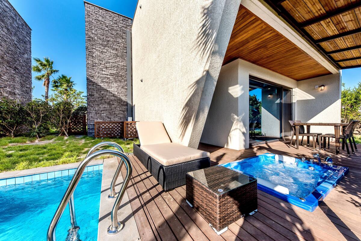 A poolside area with a hot tub, lounge chairs, and a wooden deck.