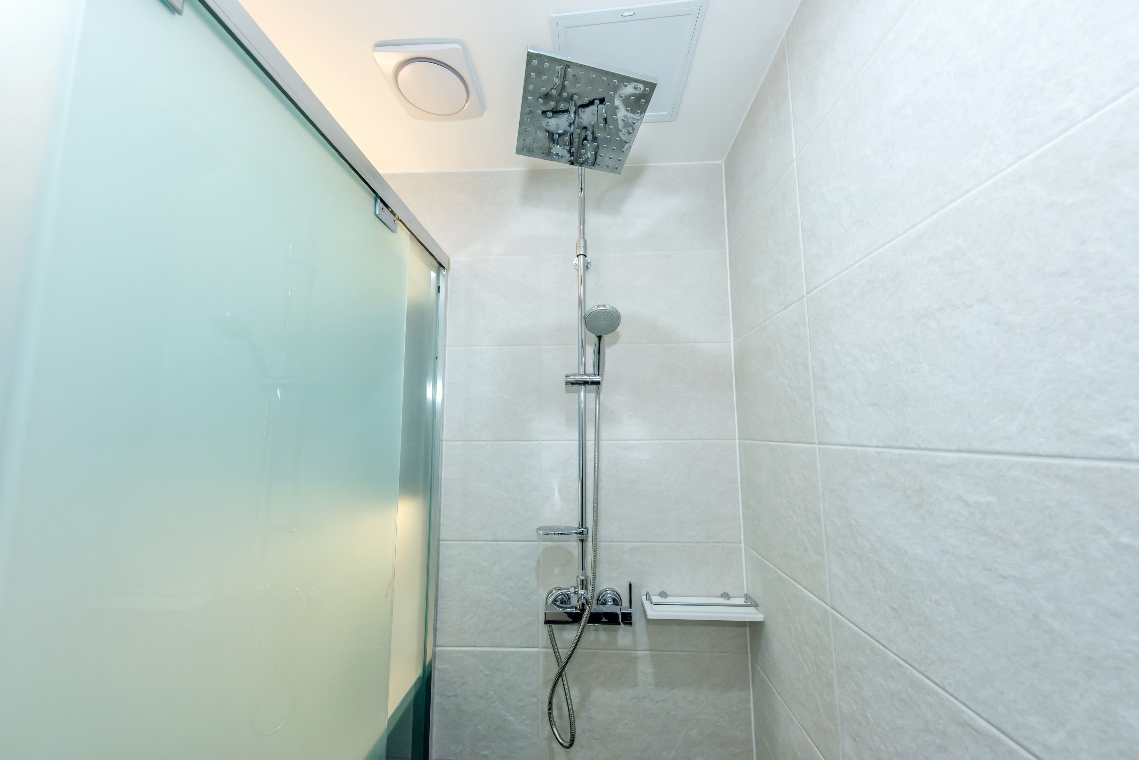 A modern bathroom with a glass shower enclosure, a handheld showerhead, and a wall-mounted faucet.