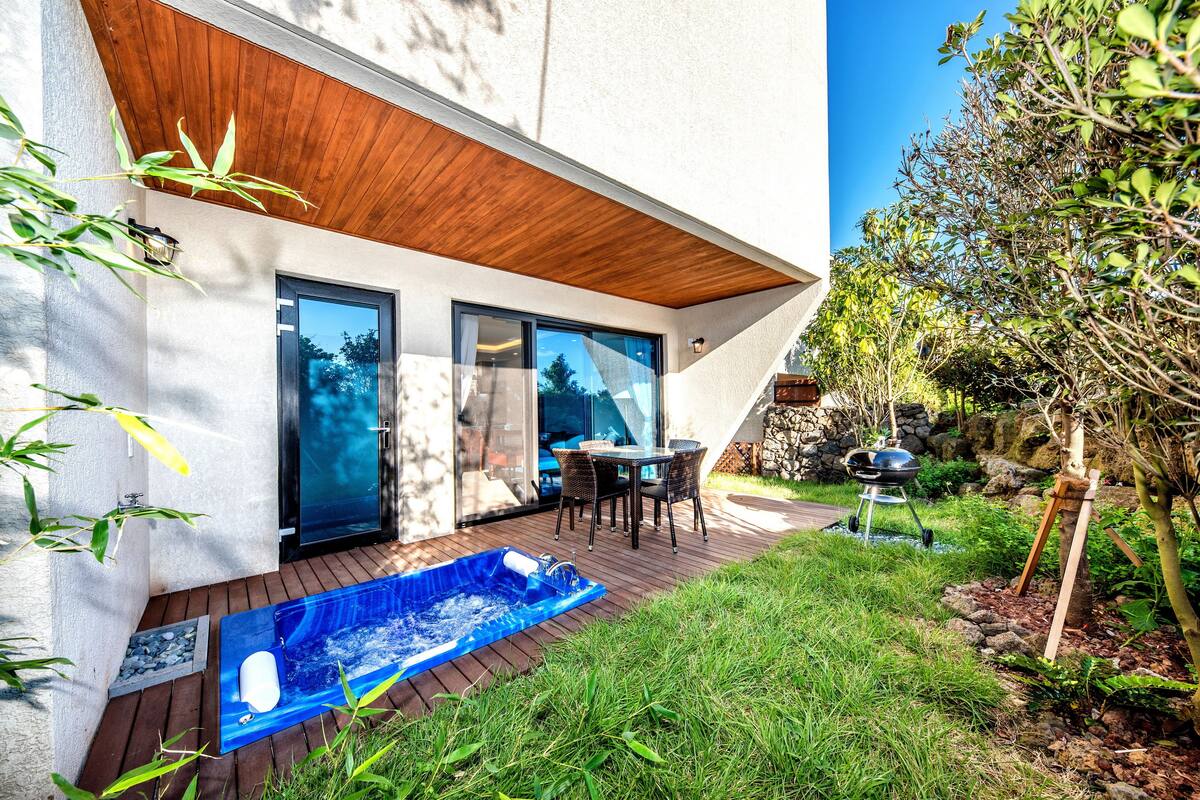 A modern house with a wooden deck, a hot tub, and a dining area with outdoor furniture.