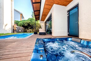 A modern outdoor hot tub area with a wooden deck, a stone wall, and a glass door. - Arts Spa & Poolvilla (Jeju City)