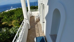 Un balcón con vistas al mar, columnas blancas y una mesa con sillas.