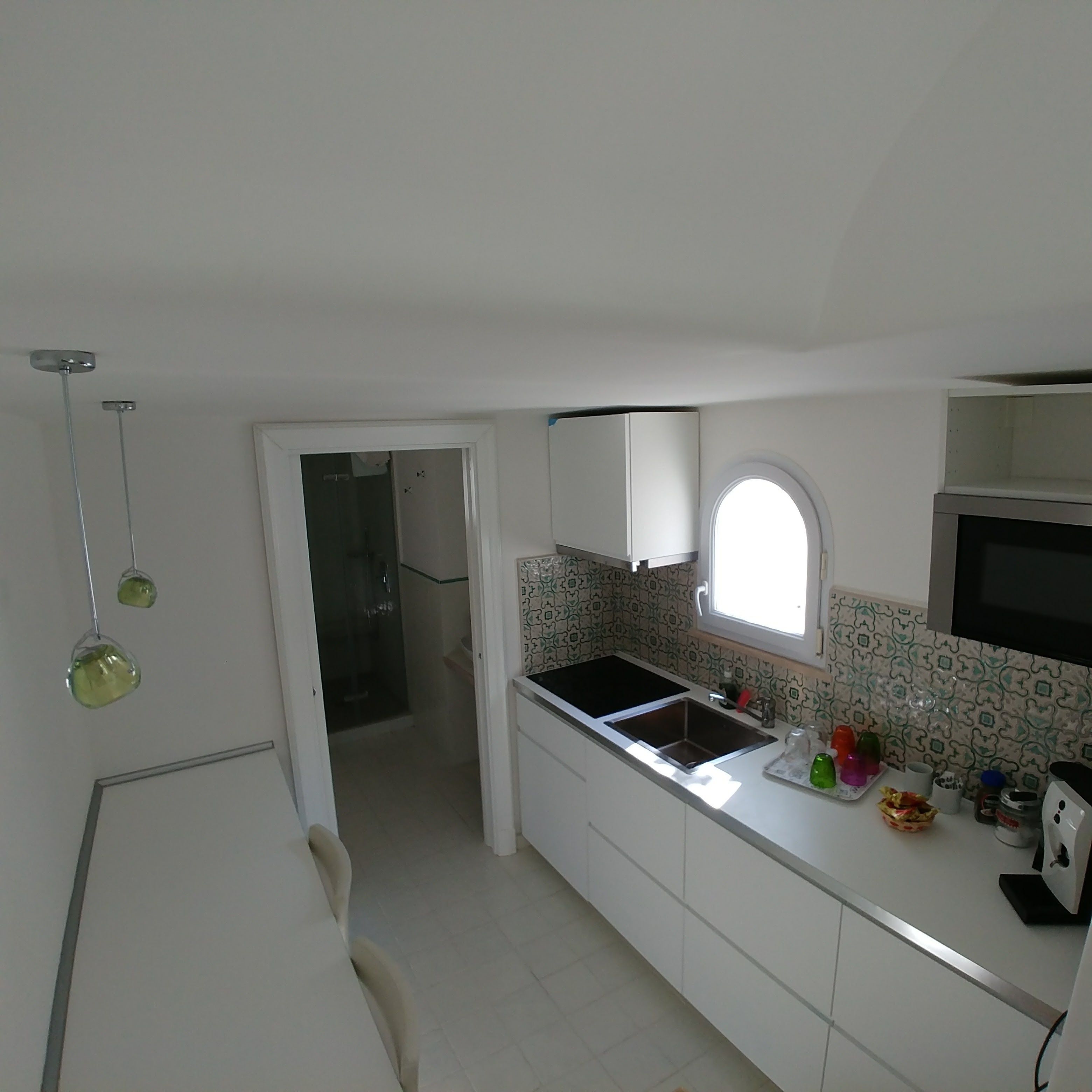 Una cocina pequeña con armarios blancos, encimera negra, una ventana y un microondas.