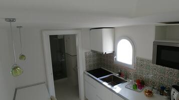 Una cocina pequeña con armarios blancos, encimera negra, una ventana y un microondas.
