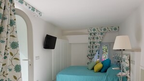 Un dormitorio con una cama, televisión, lámpara y ventana con cortinas.