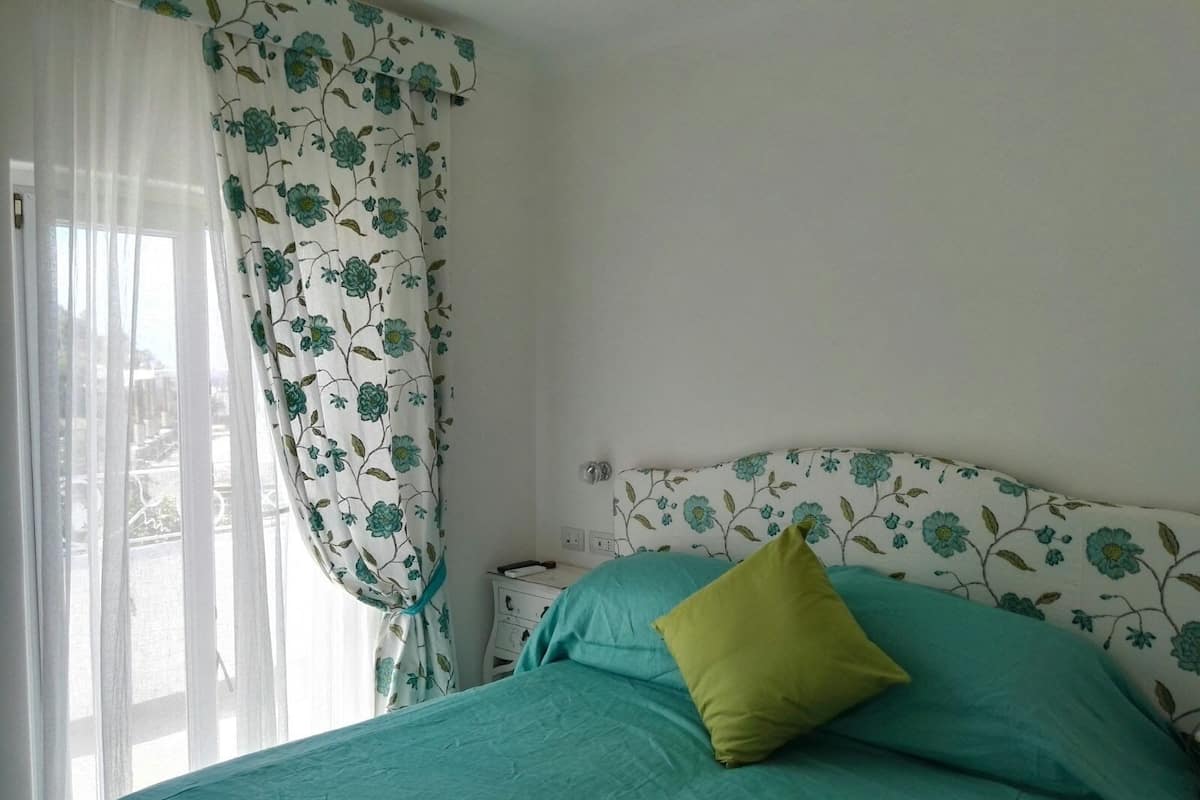 Un dormitorio con cama, mesita de noche y ventana con cortinas.