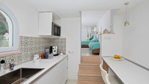 Una cocina moderna con gabinetes blancos, un microondas y un lavamanos. Se ve un pequeño comedor con una mesa y sillas al fondo.