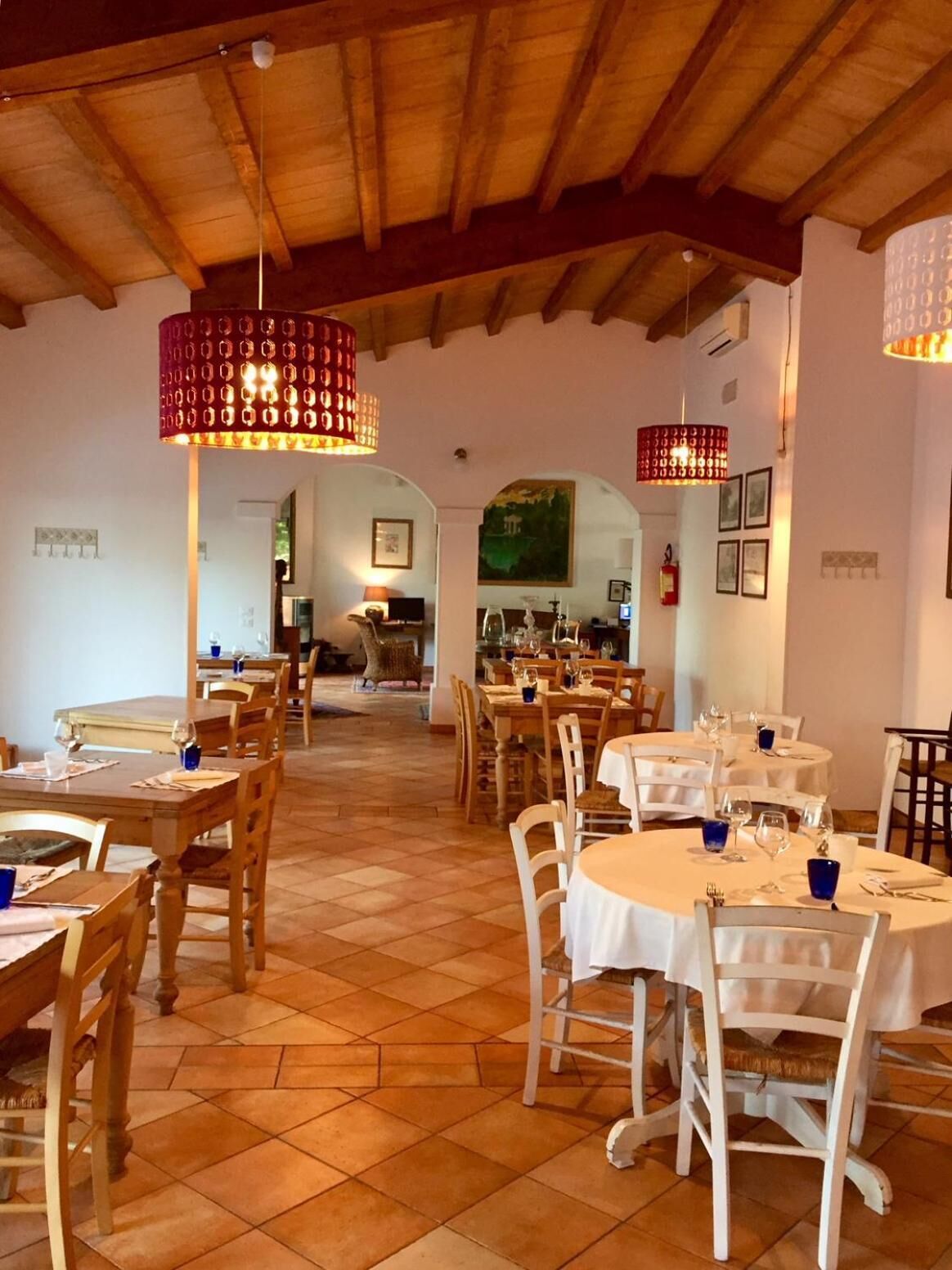 Un restaurant avec des tables et des chaises en bois, un sol carrelé et des lampes suspendues.
