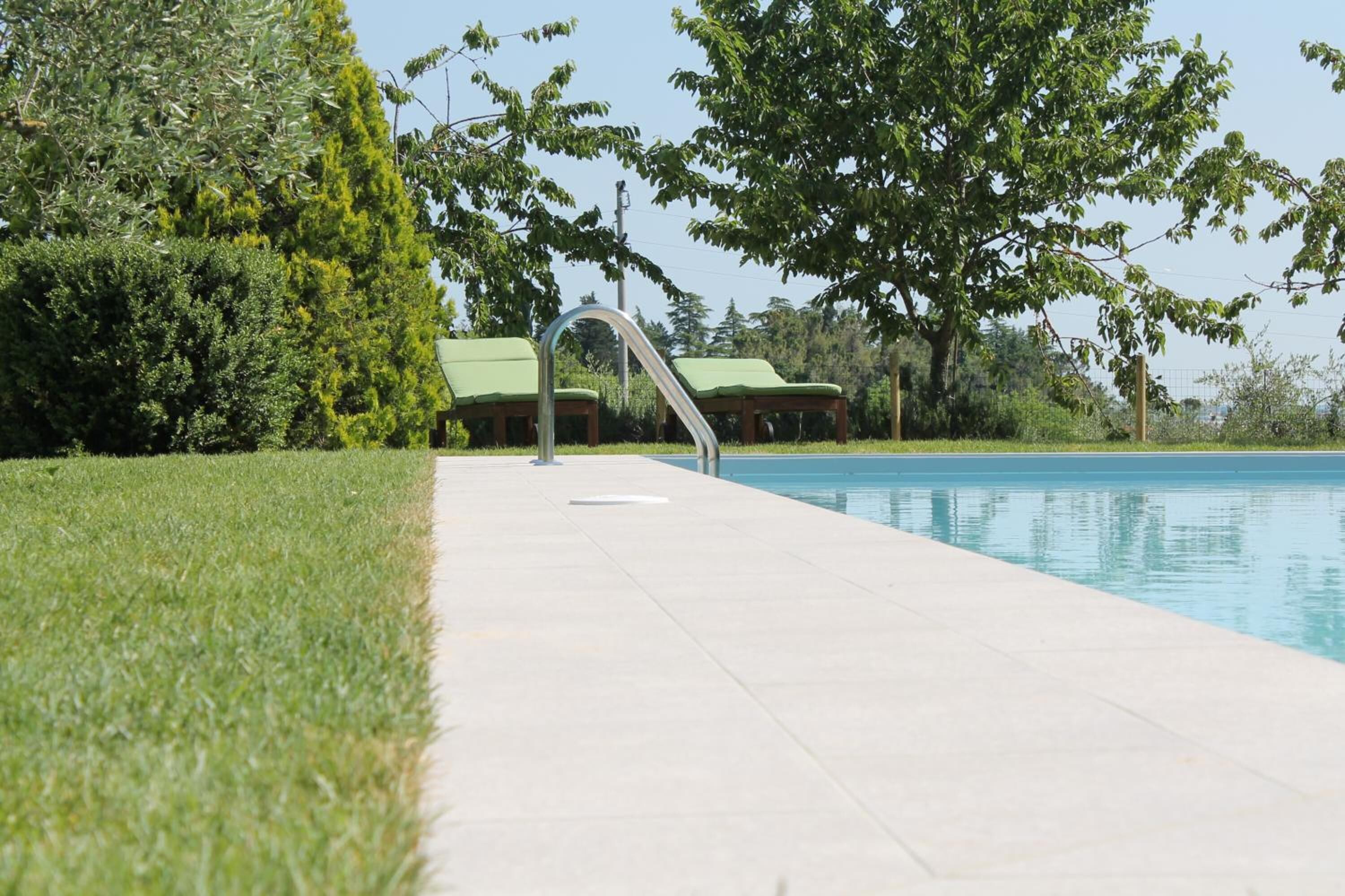 Una piscina con superficie de agua cristalina azul, rodeada por un césped cuidado y árboles.