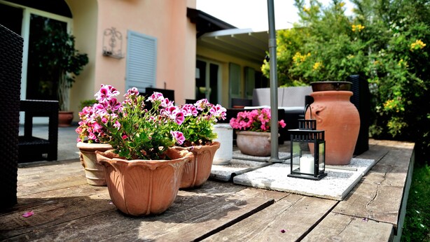 A wooden deck with terracotta pots containing pink flowers, a white lantern, and a large terracotta pot. - Agriturismo al Colle (Bertinoro)