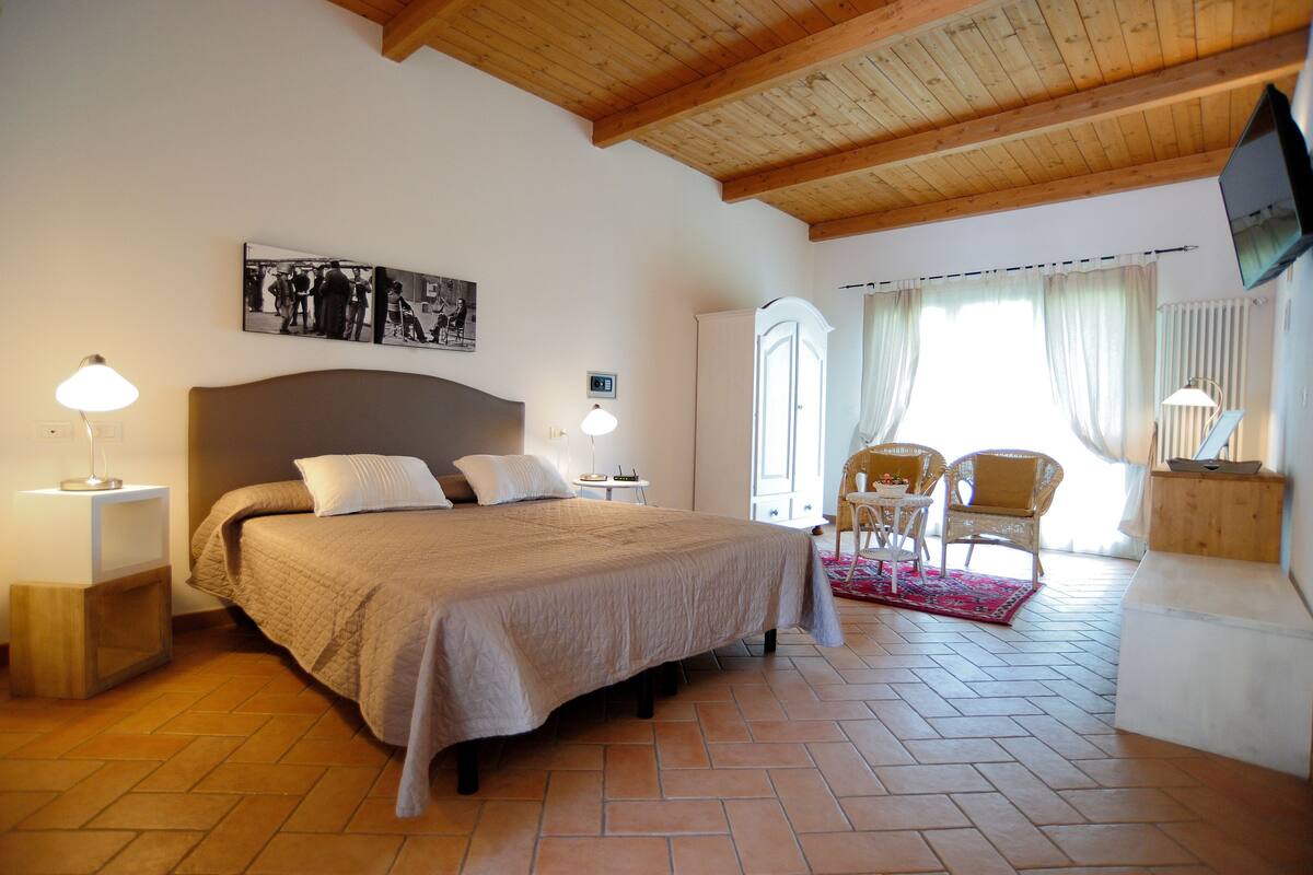A bedroom with a large bed, bedside tables, a mirror, and a view of the outside.