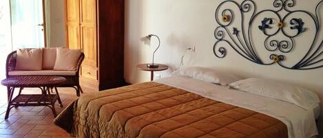 A bedroom with a large bed, a wooden wardrobe, a wicker chair, and a decorative wall piece.